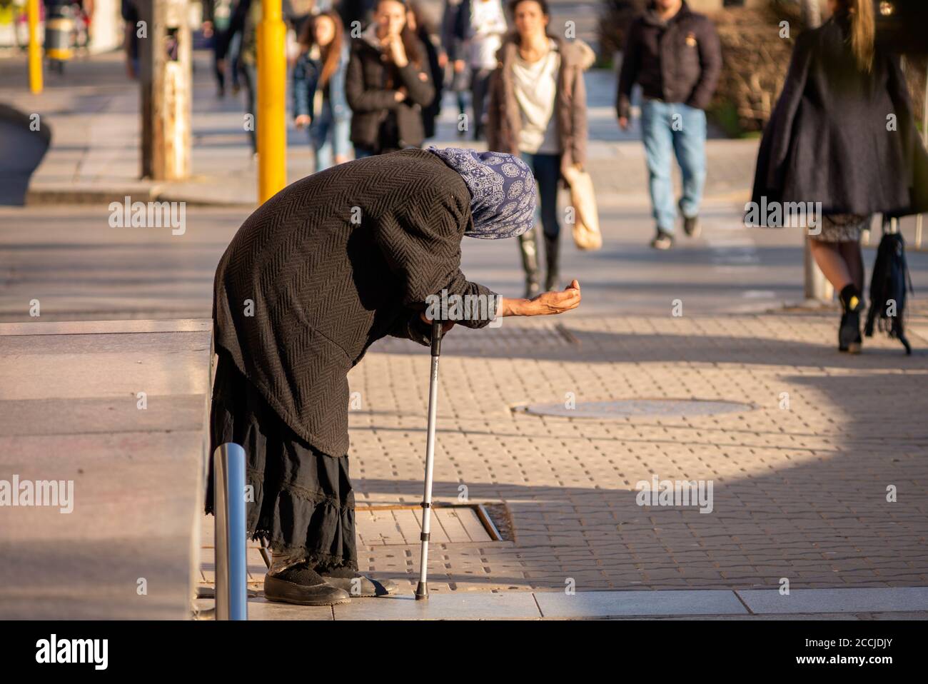 People approaching an old senior woman holding a stick and begging for money on the streets in Sofia Bulgaria Stock Photo