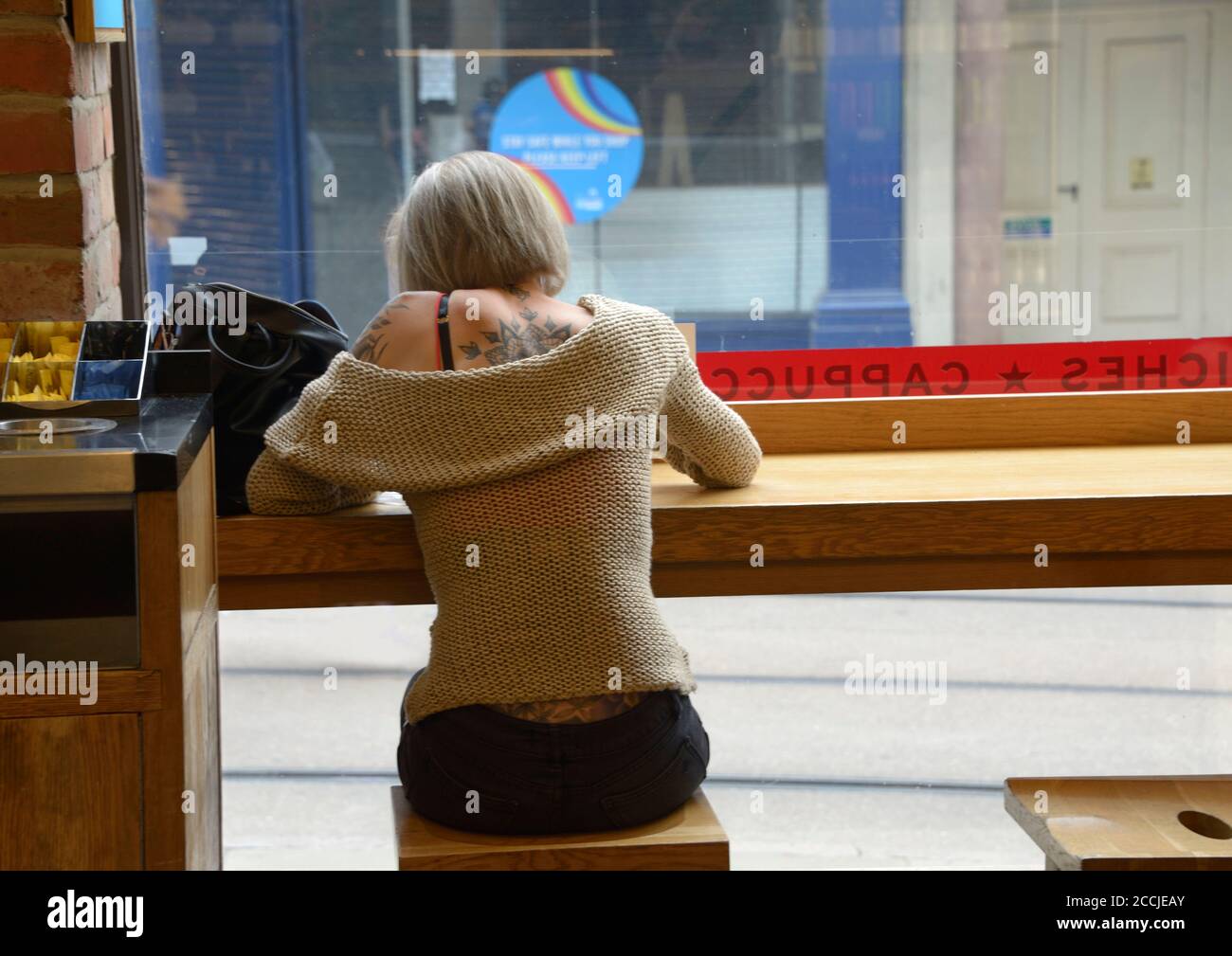 Young lady, in off shoulder sweater, showing tattoos. Sat in coffee house. Stock Photo
