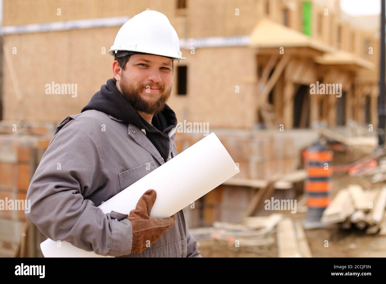 Caucasian builder holding architecture drawing plan on paper at construction site. Stock Photo