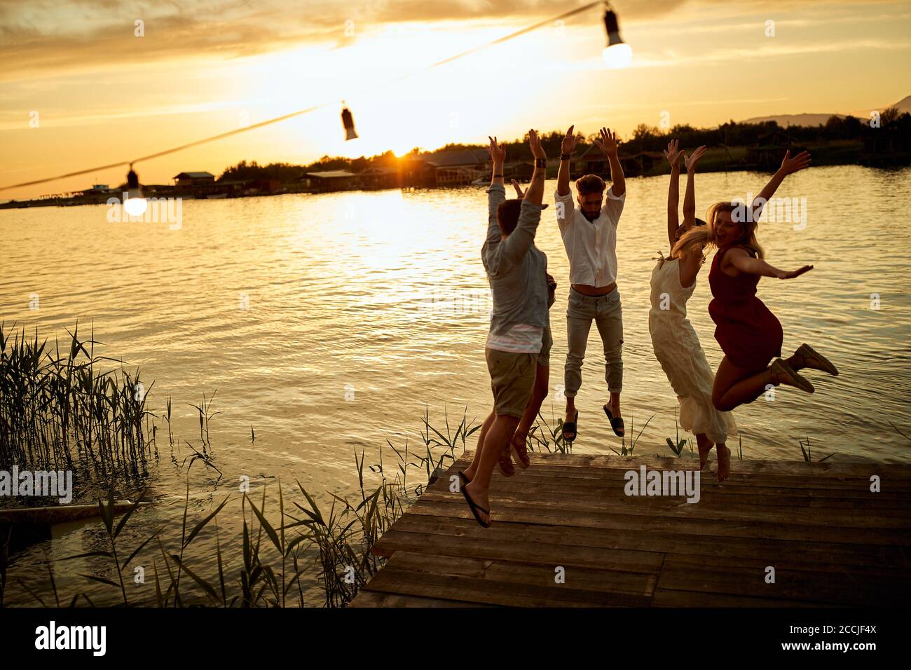 Group of friends jumping on the shore of the lake on the sunset Stock Photo