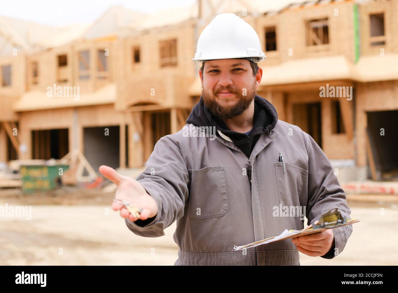 Bearded builder giving apartment keys and holding drawing plan in notebook. Stock Photo