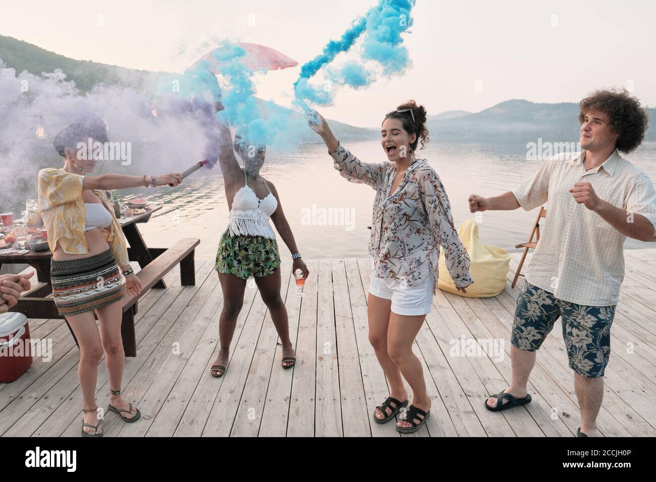 Group of teenagers dancing on a pier outdoors among colored smoke Stock Photo