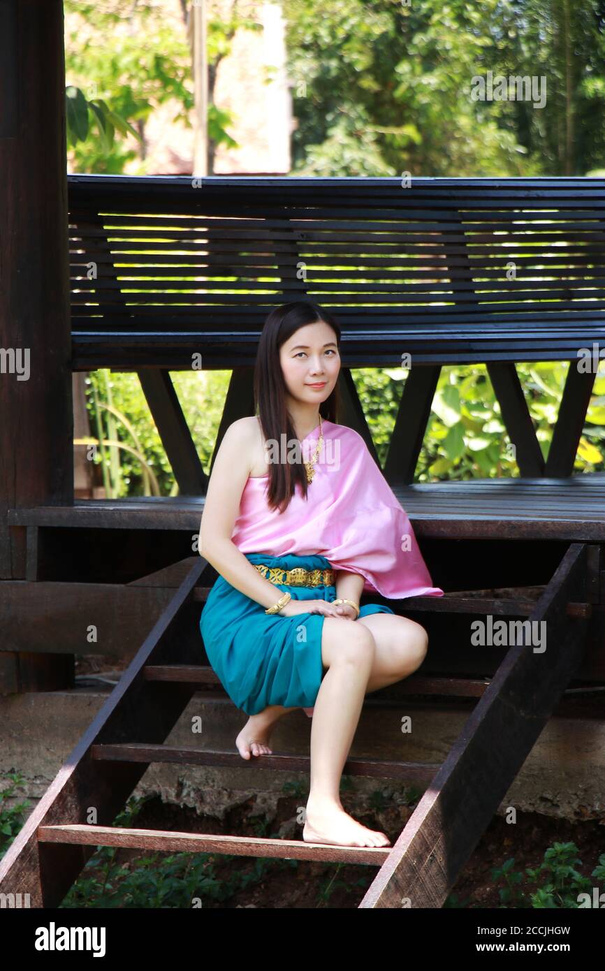 Thai Asian polite woman with smile face in traditional costume of Thailand at waterfront pavilion front of riverside ancient house near the river. Bea Stock Photo
