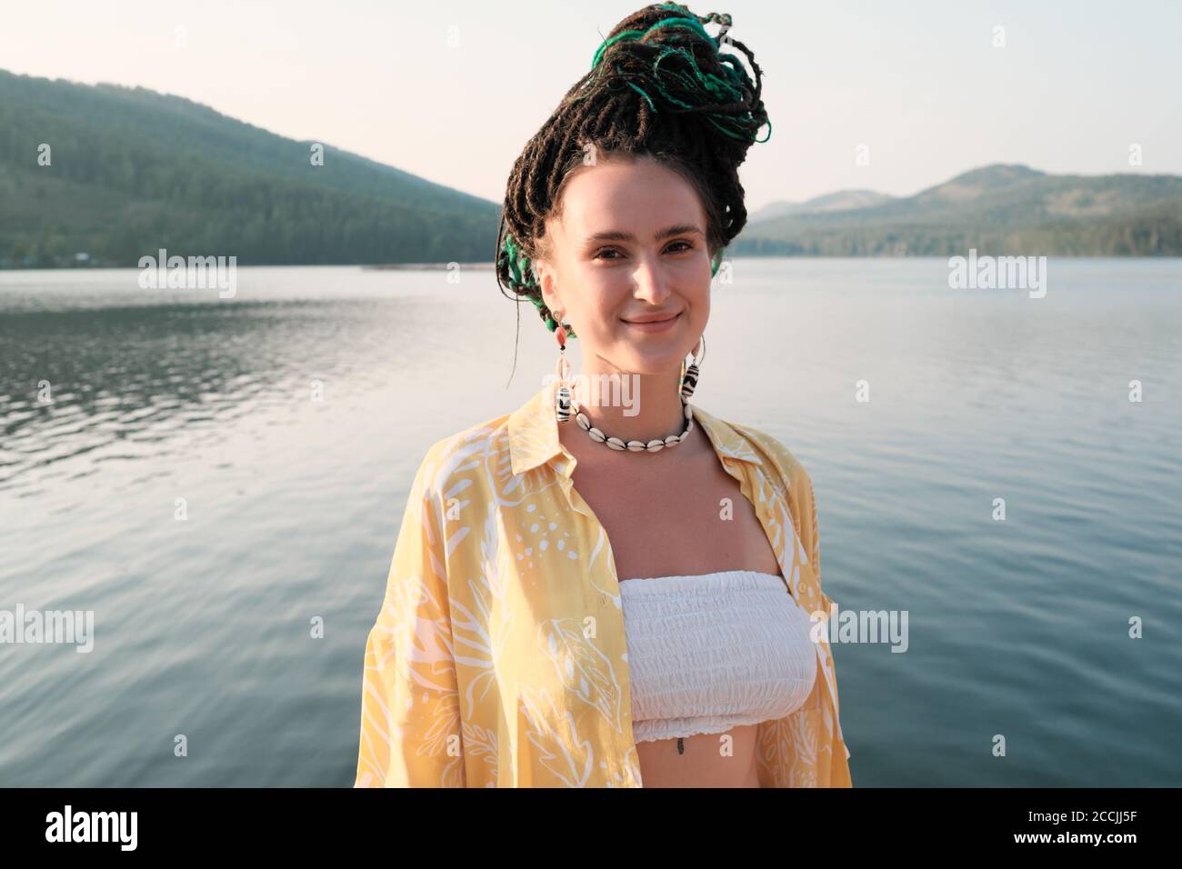 Portrait of young woman with fashion hairstyle looking at camera with beautiful view of the lake behind her Stock Photo