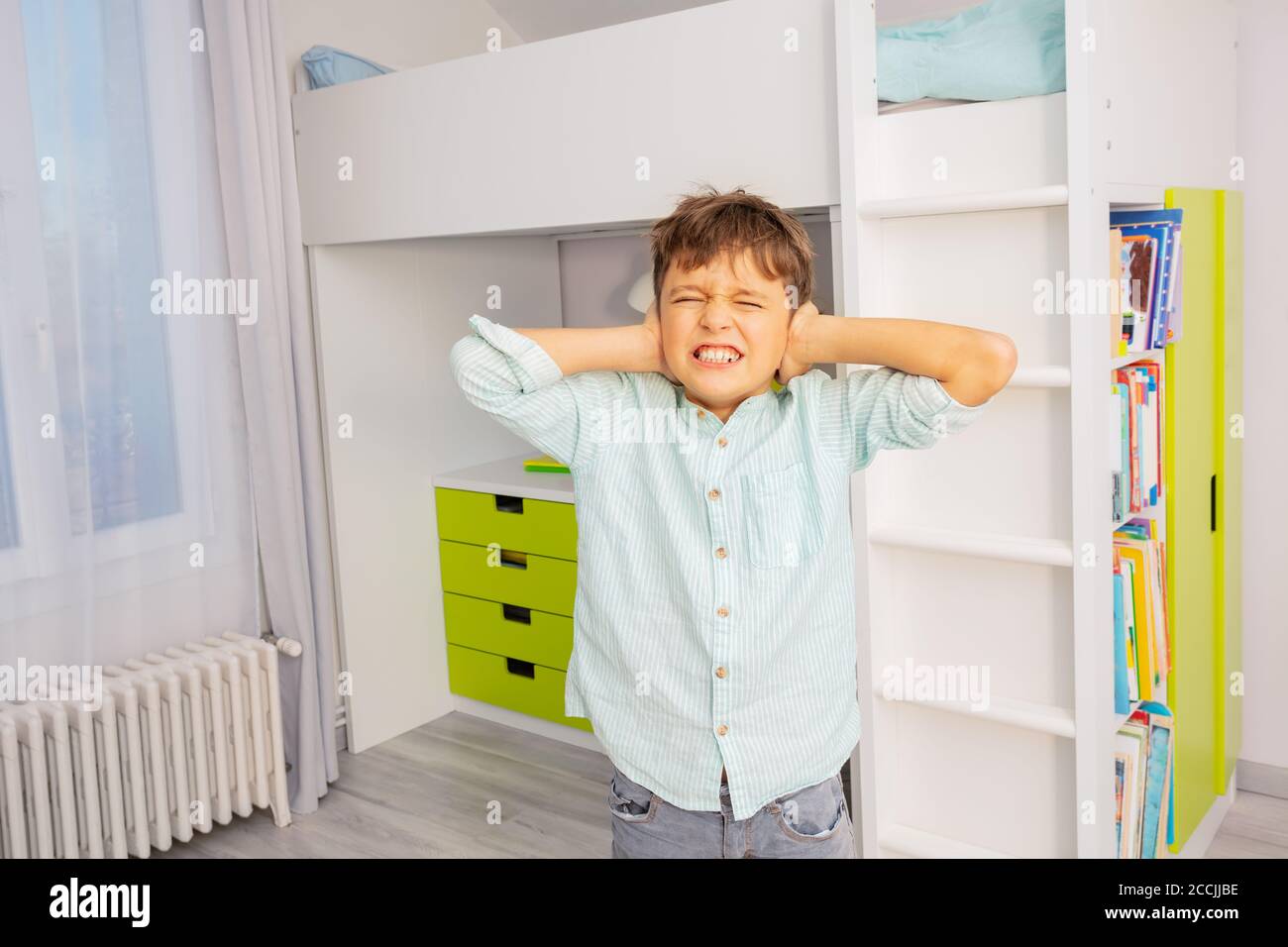 Little autistic boy with strong negative face expression closing ears and grins teeth Stock Photo