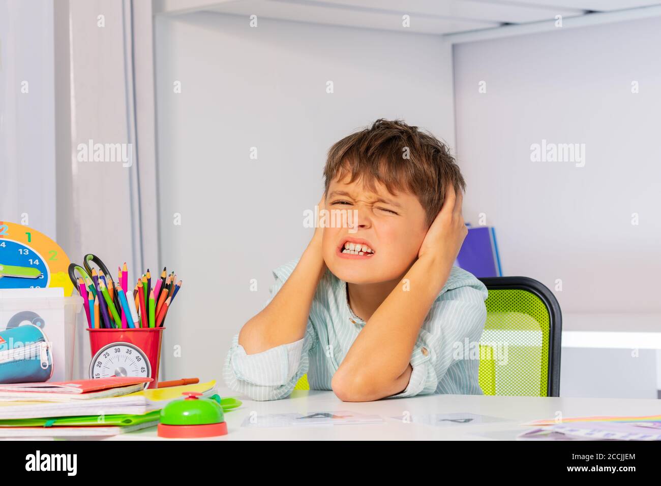 Screaming sad boy with autistic disorder cover ears and grin during development therapy class lesson Stock Photo