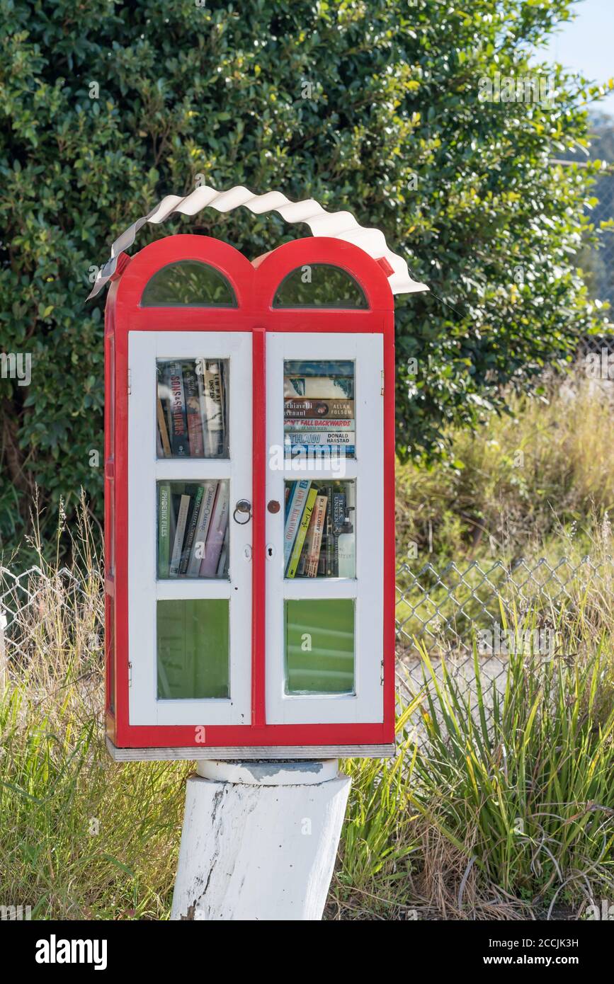 A colourful red and white mini street library mounted on a timber pylon near a public wharf at Brooklyn, New South Wales, Australia Stock Photo