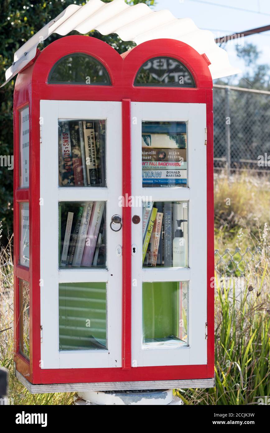 A colourful red and white mini street library mounted on a timber pylon ...