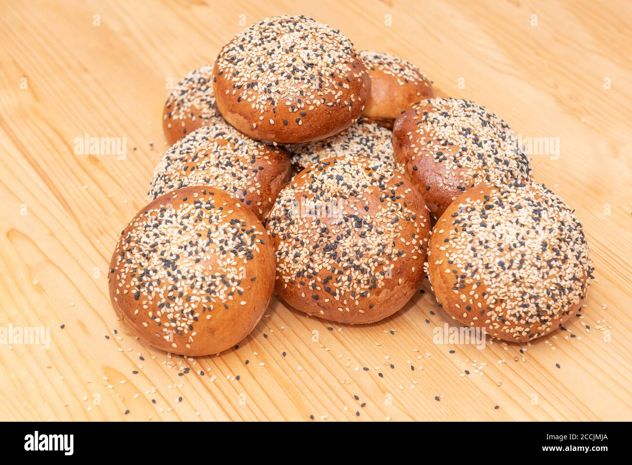 stack of small brown breads with white and black sesame on wooden table, used for burgers Stock Photo