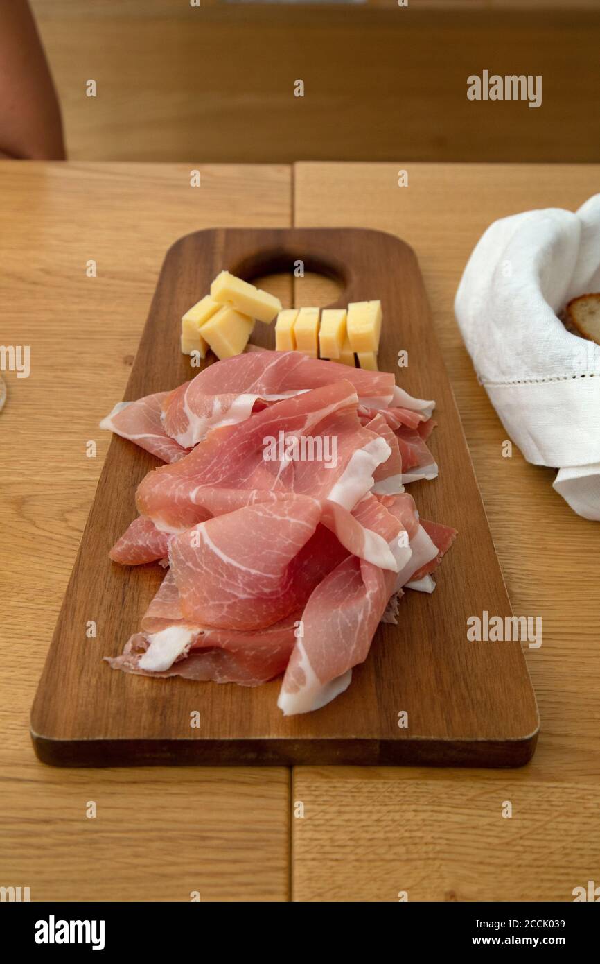 A wooden bread board with prosciutto ham and local cheese at a restaurant in Slovenia. Stock Photo