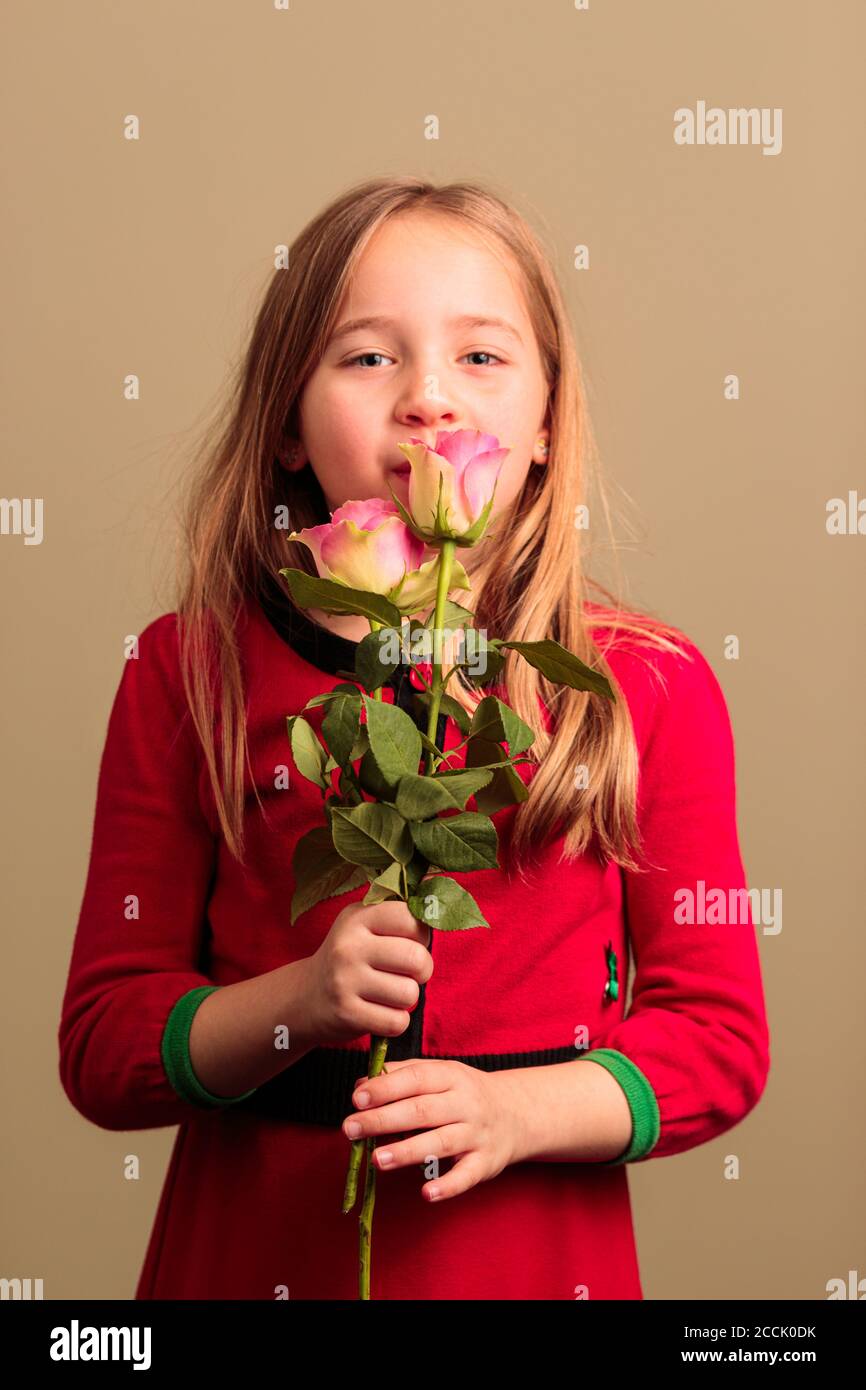 Young pretty 8 year old girl wearing a red dress smelling flowers ...