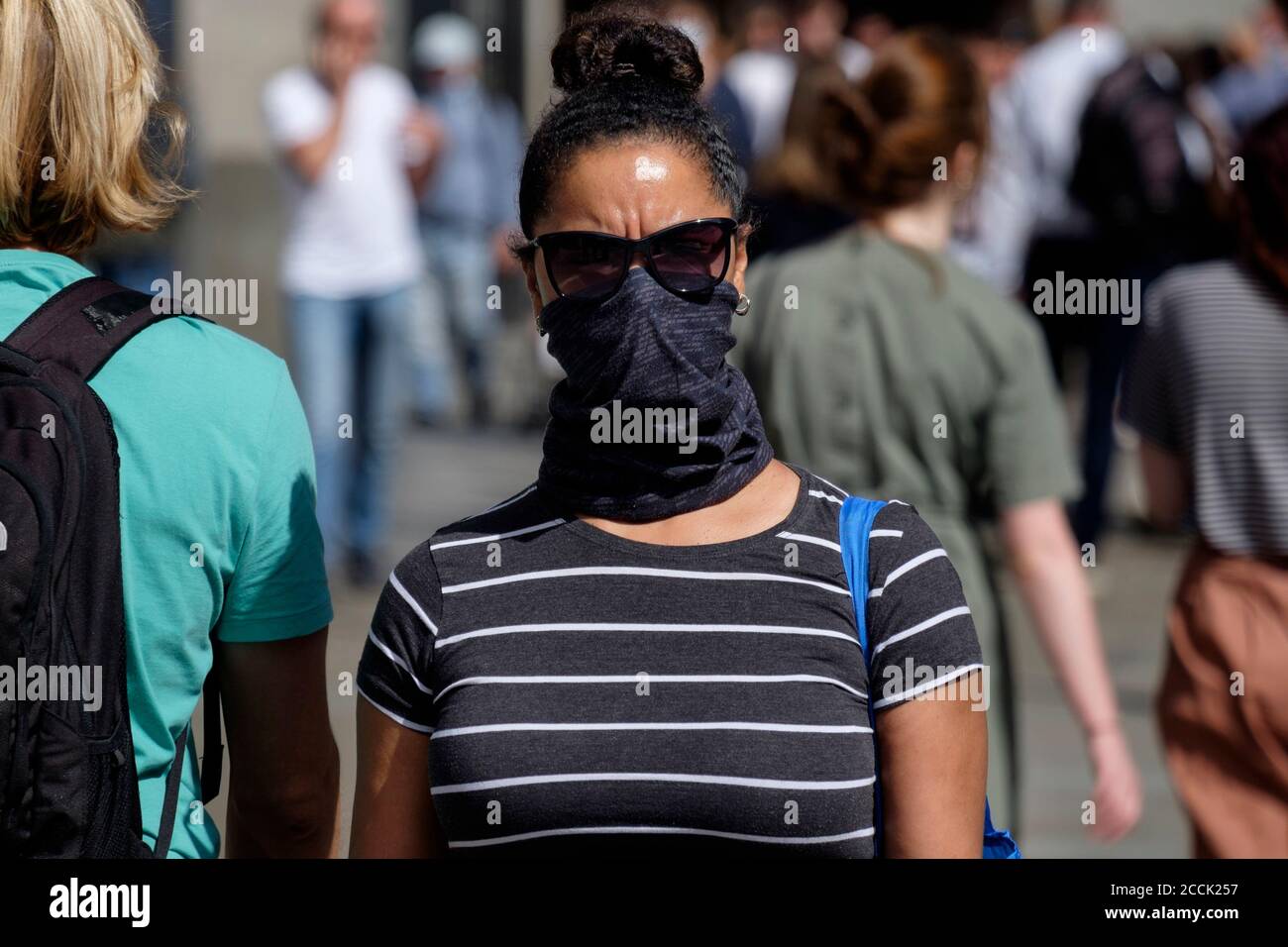 African Caribbean woman wearing bandana style scarf as face covering on busy street. Stock Photo