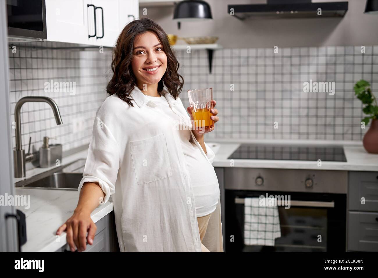 portrait of happy pregnant lady drinking fresh juice in the kitchen ...
