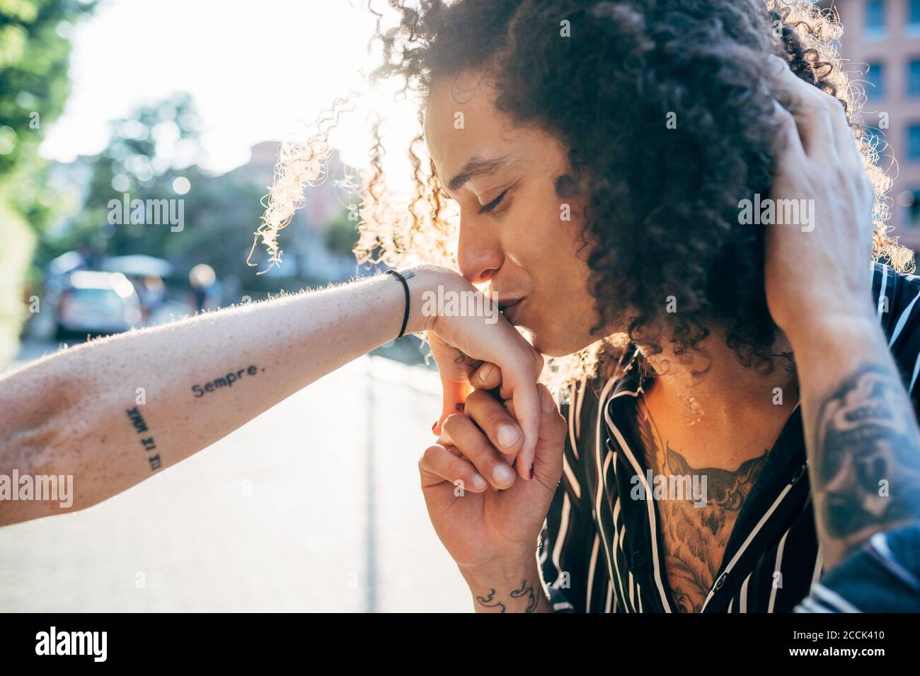 Close-up of loving man with curly hair kissing on girlfriend's hand in city Stock Photo