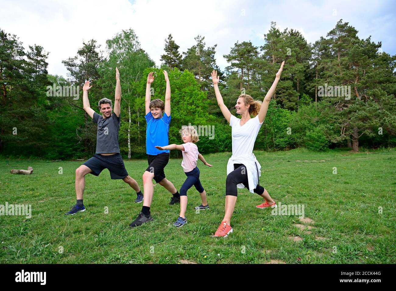 Family practicing warrior poses on grassy land in forest Stock Photo
