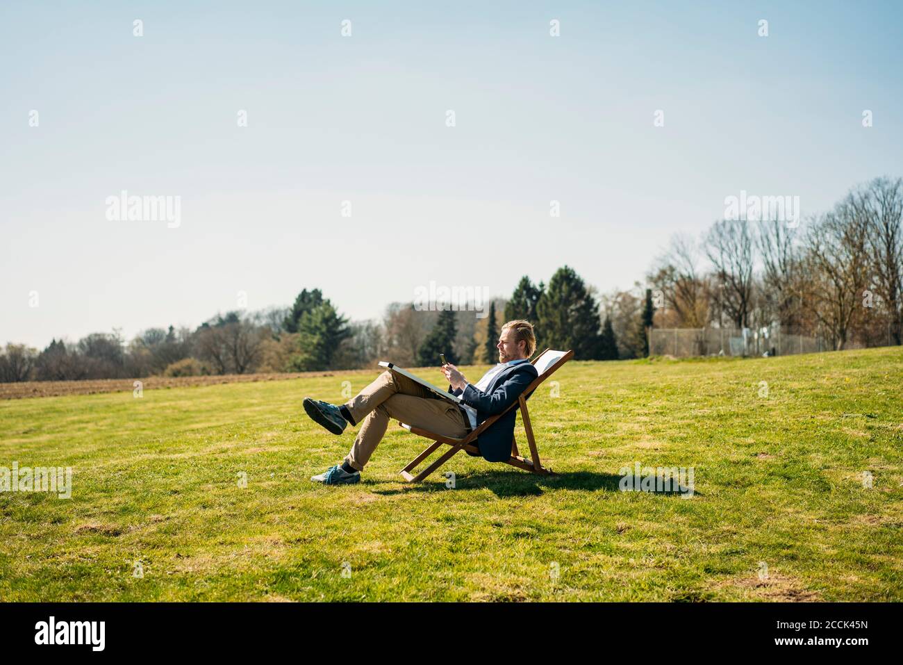 Mature male professional using smart phone while sitting on chair with solar panel at park during sunny day Stock Photo