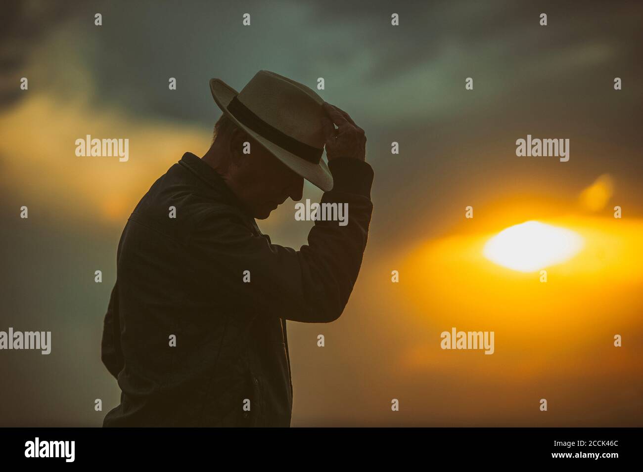 Senior man bowing in front of setting sun Stock Photo