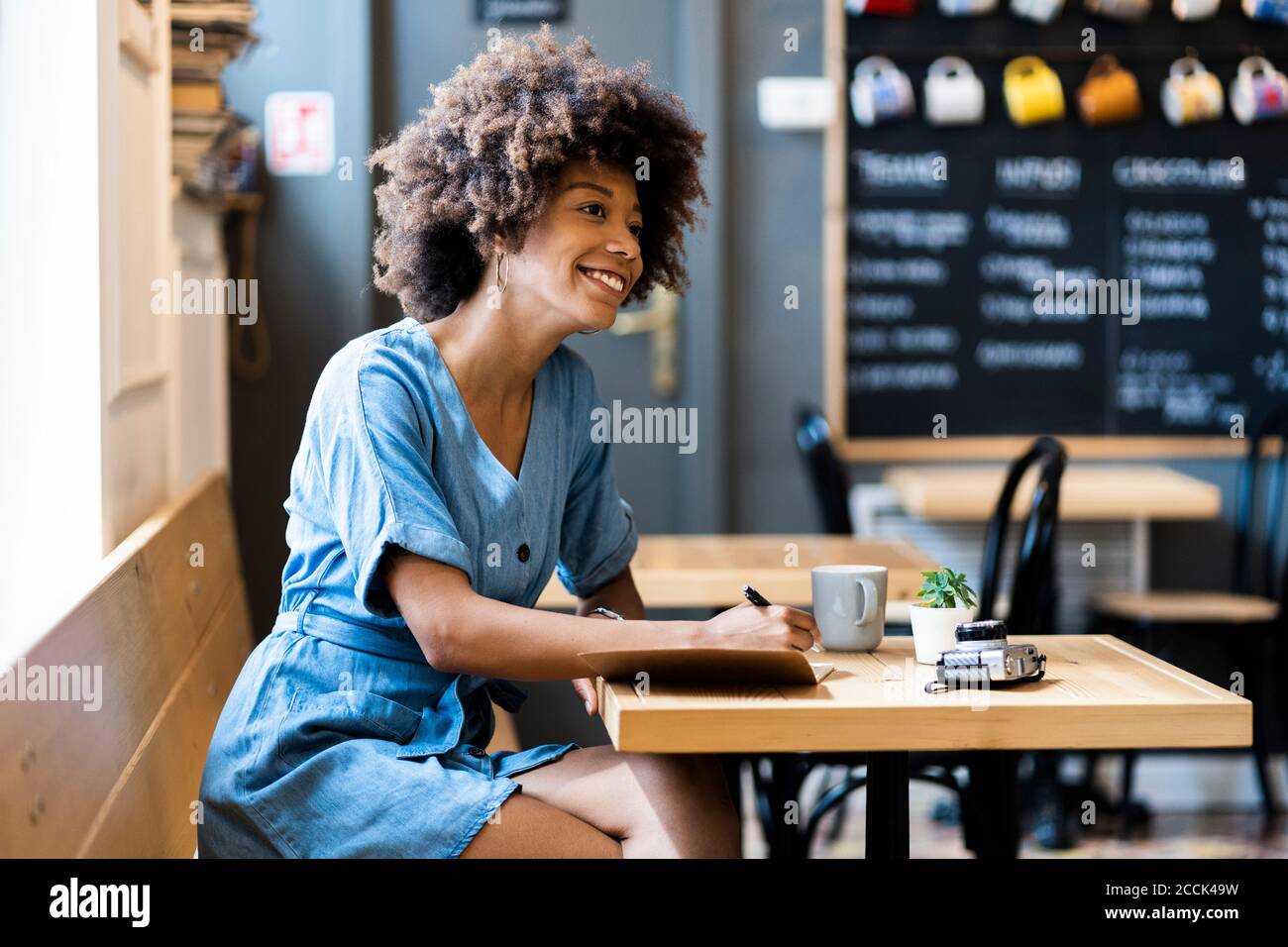 Thoughtful woman writing in book while sitting at table in coffee shop Stock Photo