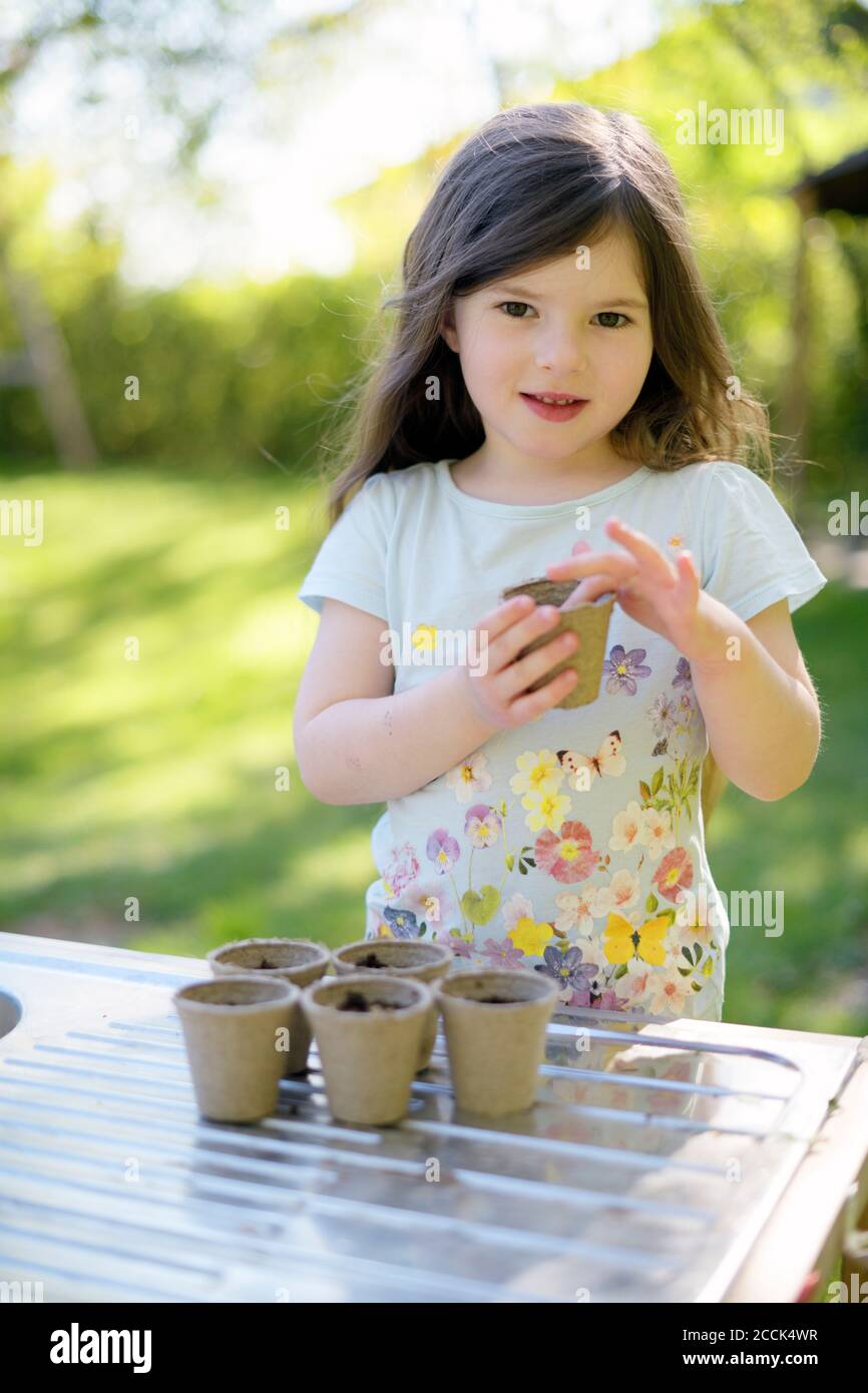 Cute girl planting seeds in small pots on table at yard Stock Photo
