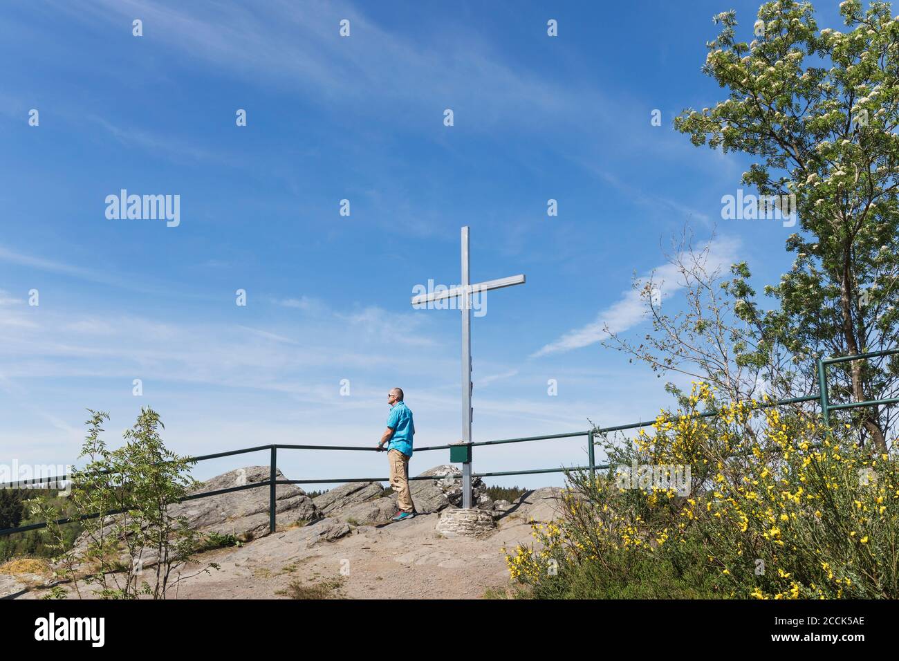 Germany, North Rhine-Westphalia, Monschau, Man admiring views by cross standing on summit of Ehrensteinley Stock Photo