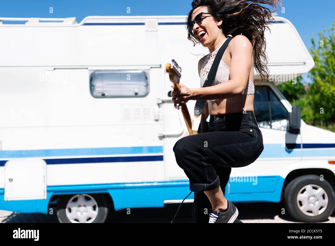 Happy young woman playing electric guitar infront of a camper Stock Photo