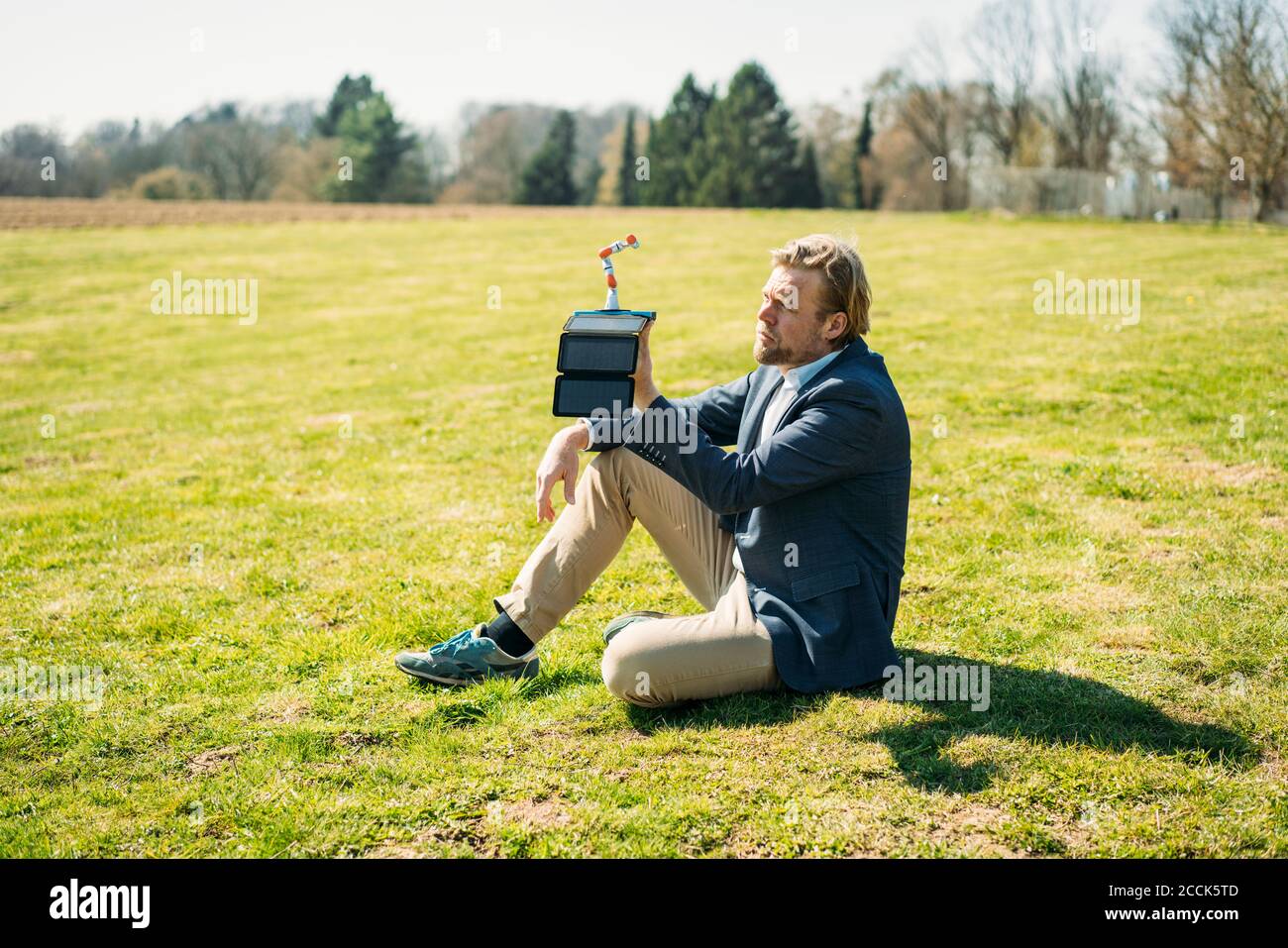 Businessman analyzing robot arm while charging with portable solar panel at park on sunny day Stock Photo