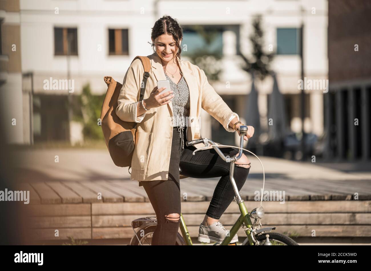 Female student using mobile phone while sitting on bicycle in city during sunny day Stock Photo
