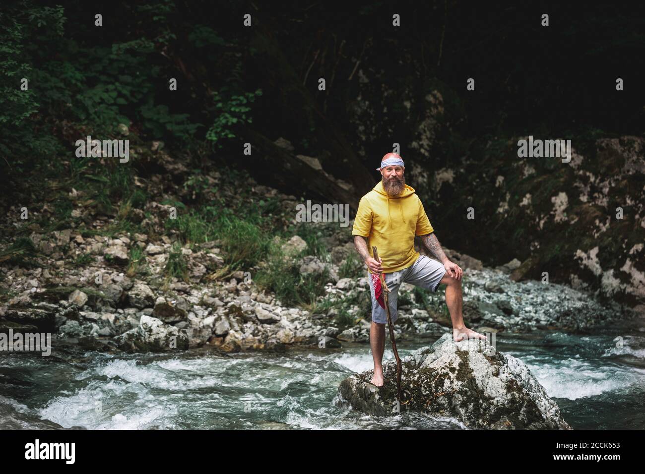 Adventurer with beard sitting in the middle of river on stone and carving on piece of wood Stock Photo