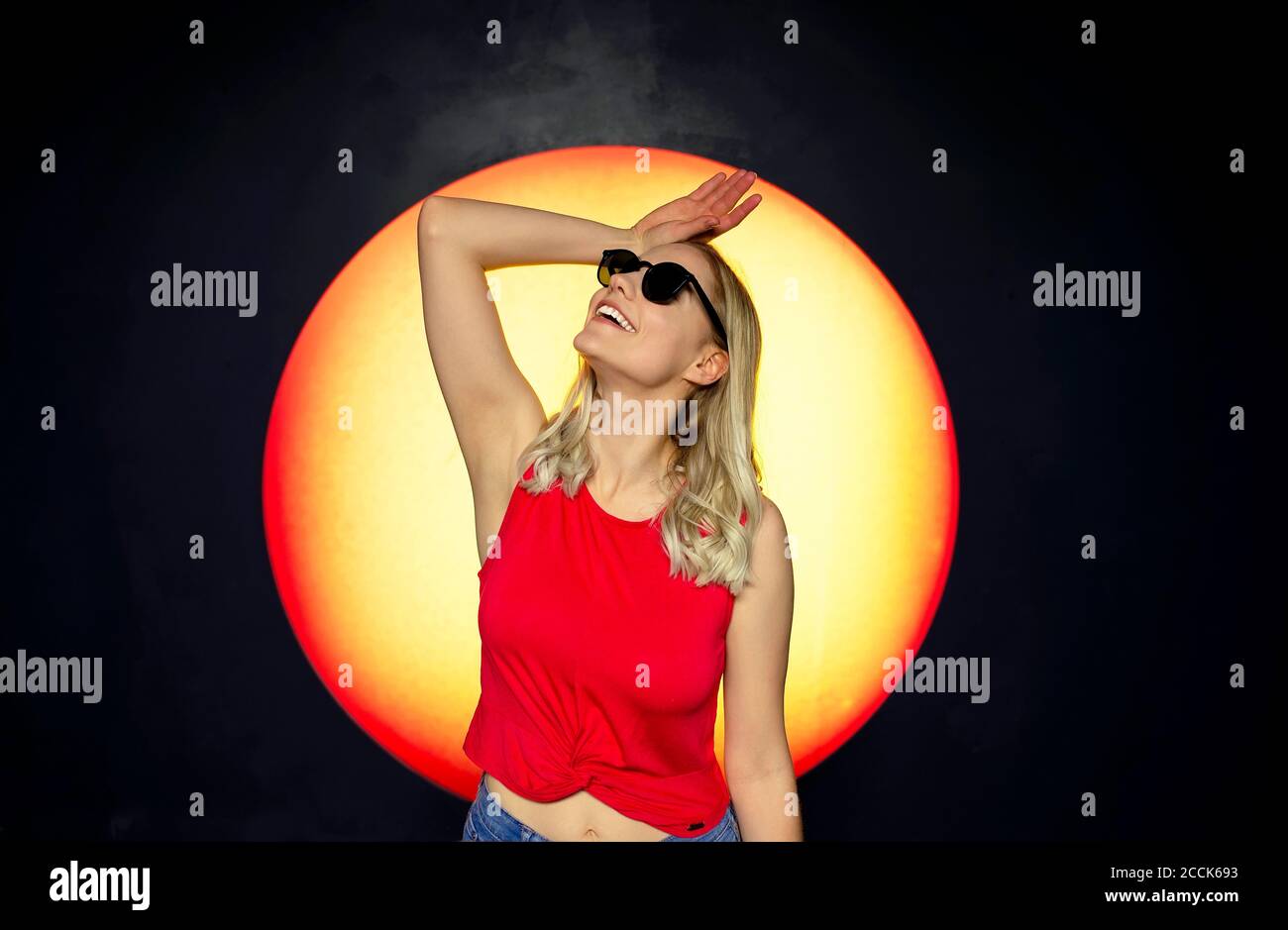 Smiling beautiful woman wearing sunglasses posing against backdrop of sunset Stock Photo