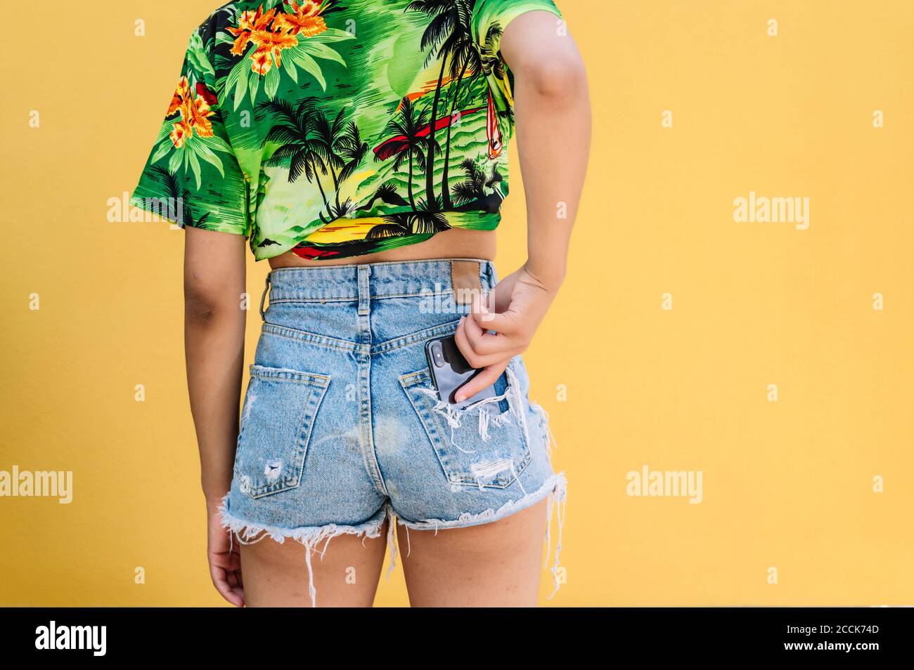 Rear view of young woman putting smartphone in pocket of jeans shorts Stock Photo