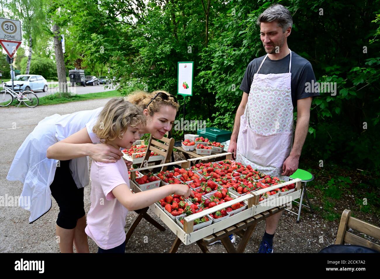 Male vendor looking at mother and daughter choosing strawberries at market stall Stock Photo