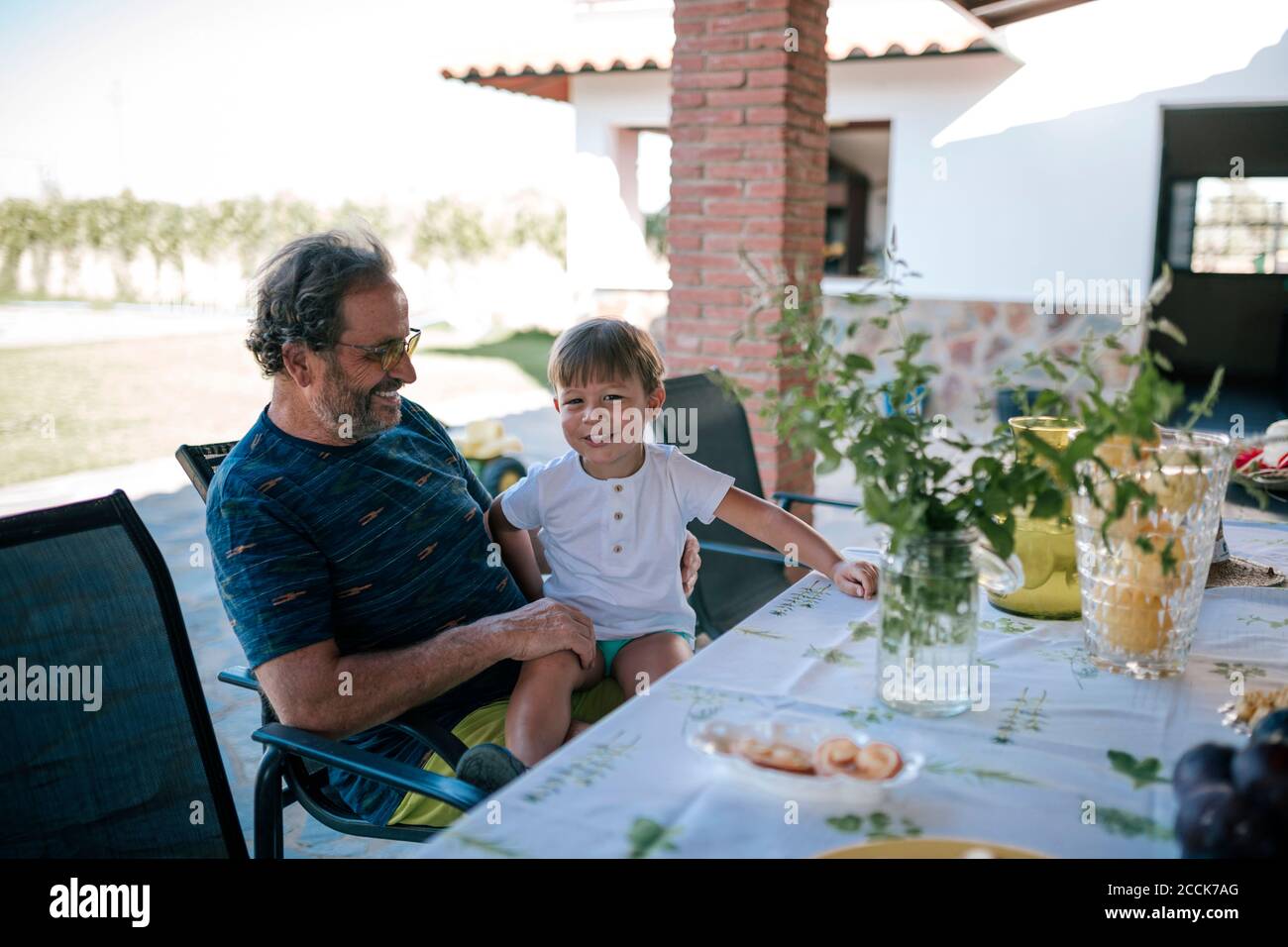 Grandfather and grandchild sitting on chair at dinning table outside house Stock Photo