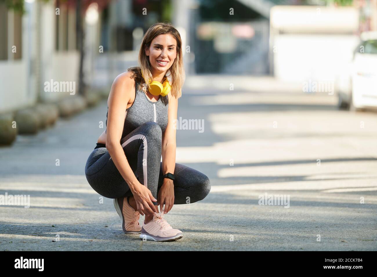 Smiling woman with headphones tying shoelace at sidewalk Stock Photo