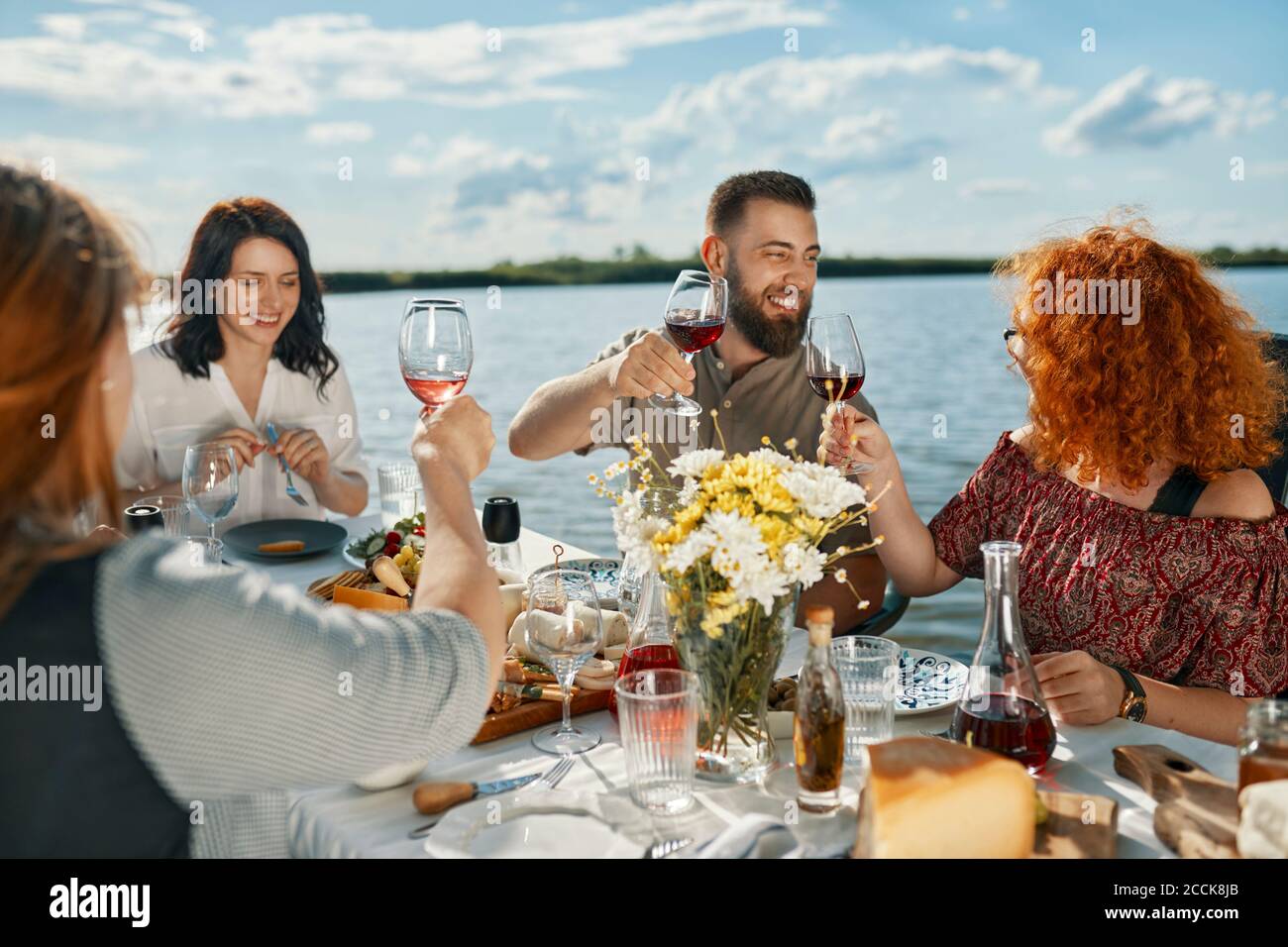 Friends having dinner at a lake rasing wine glasses Stock Photo