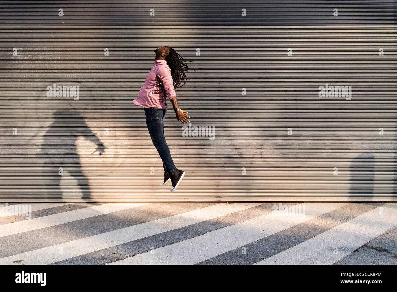 Carefree young man with dreadlocks jumping on street against wall Stock Photo