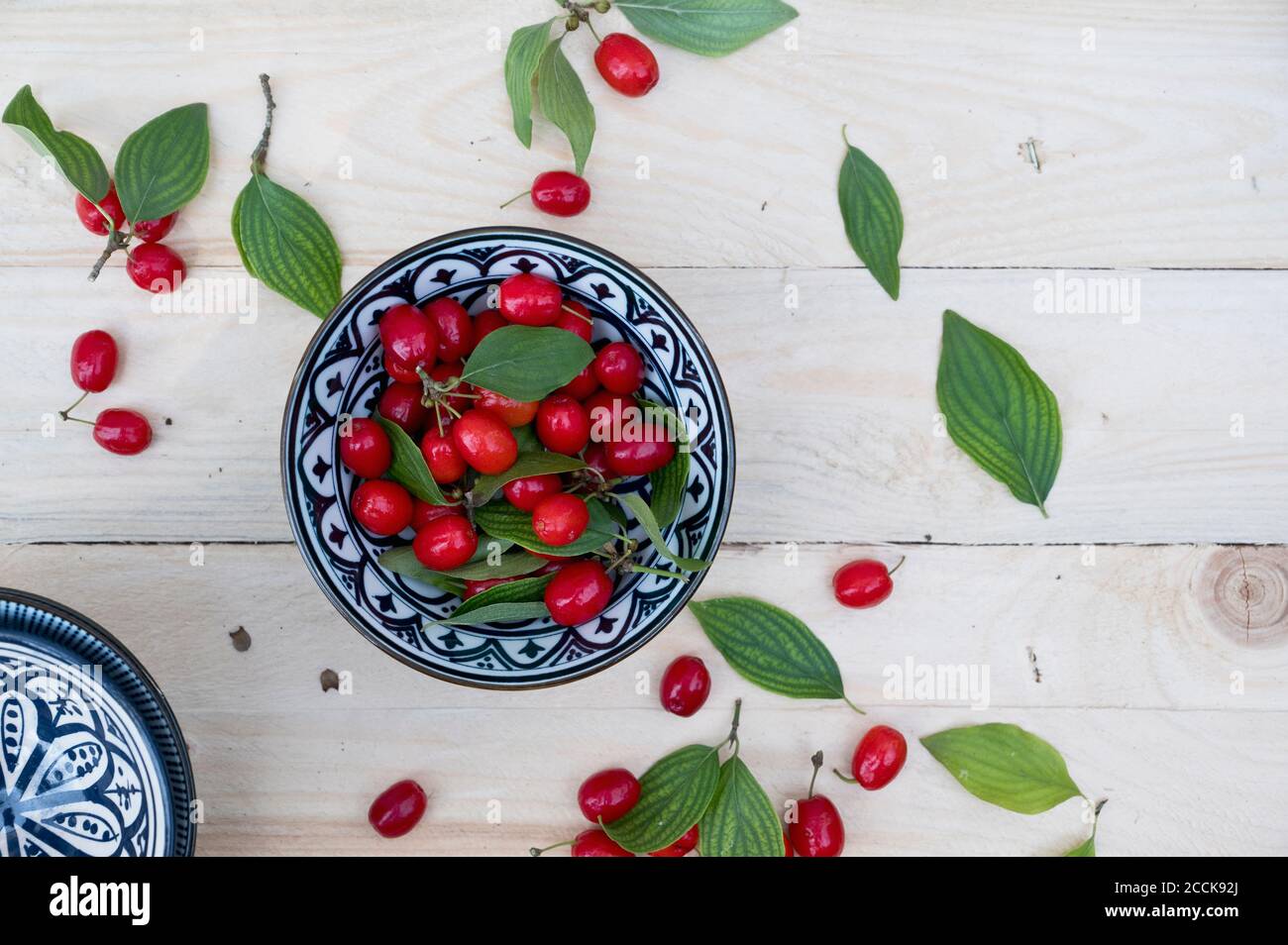 Bowl with leaves and fresh Cornelian cherries (Cornus mas) Stock Photo
