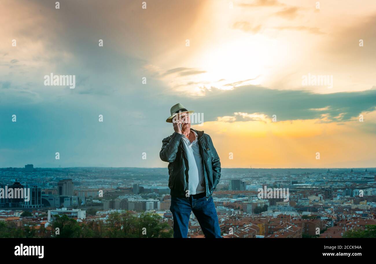 Senior man talking on mobile phone with city in background during sunset Stock Photo