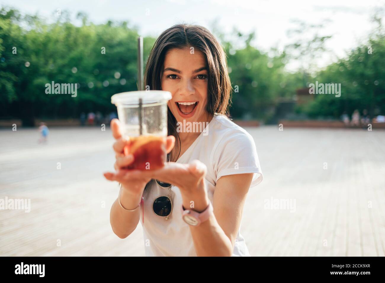 Cheerful young woman with mouth open holding soft drink cup while standing in park Stock Photo