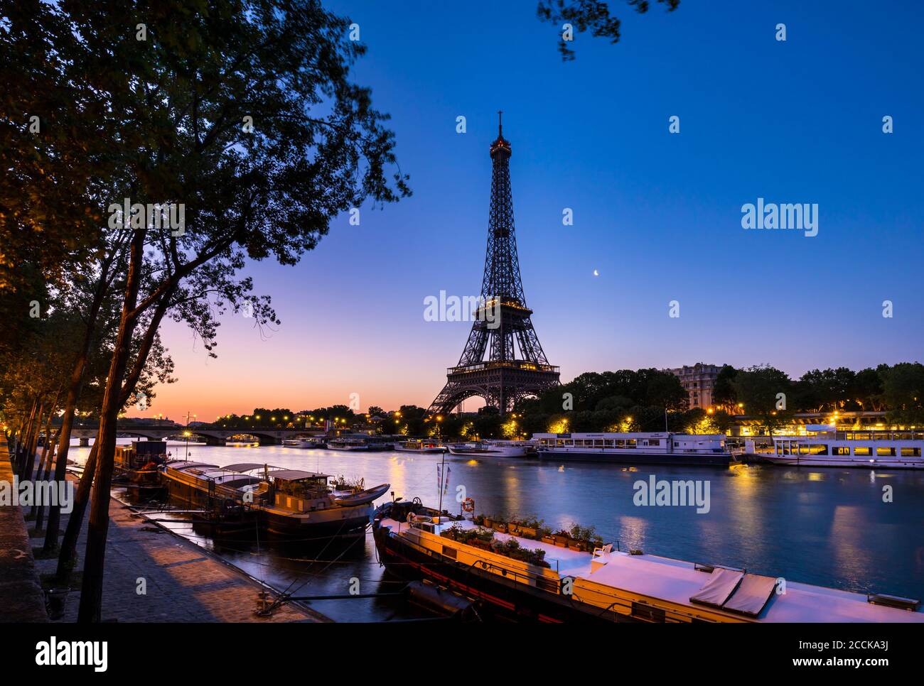 Eiffel Tower by Seine river against clear blue sky at sunset, Paris, France Stock Photo