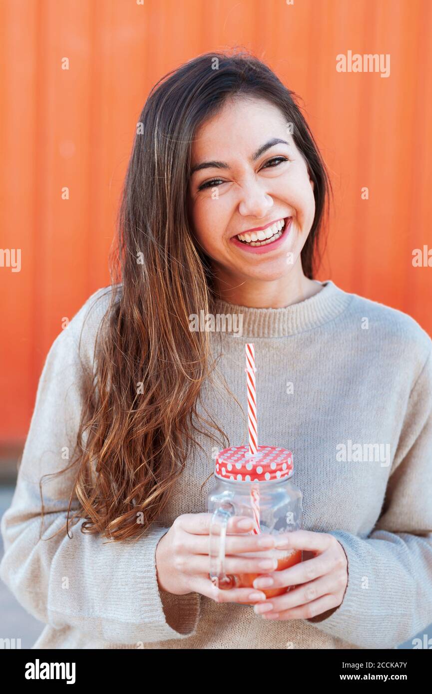 Cheerful young woman with long brown holding drink Stock Photo