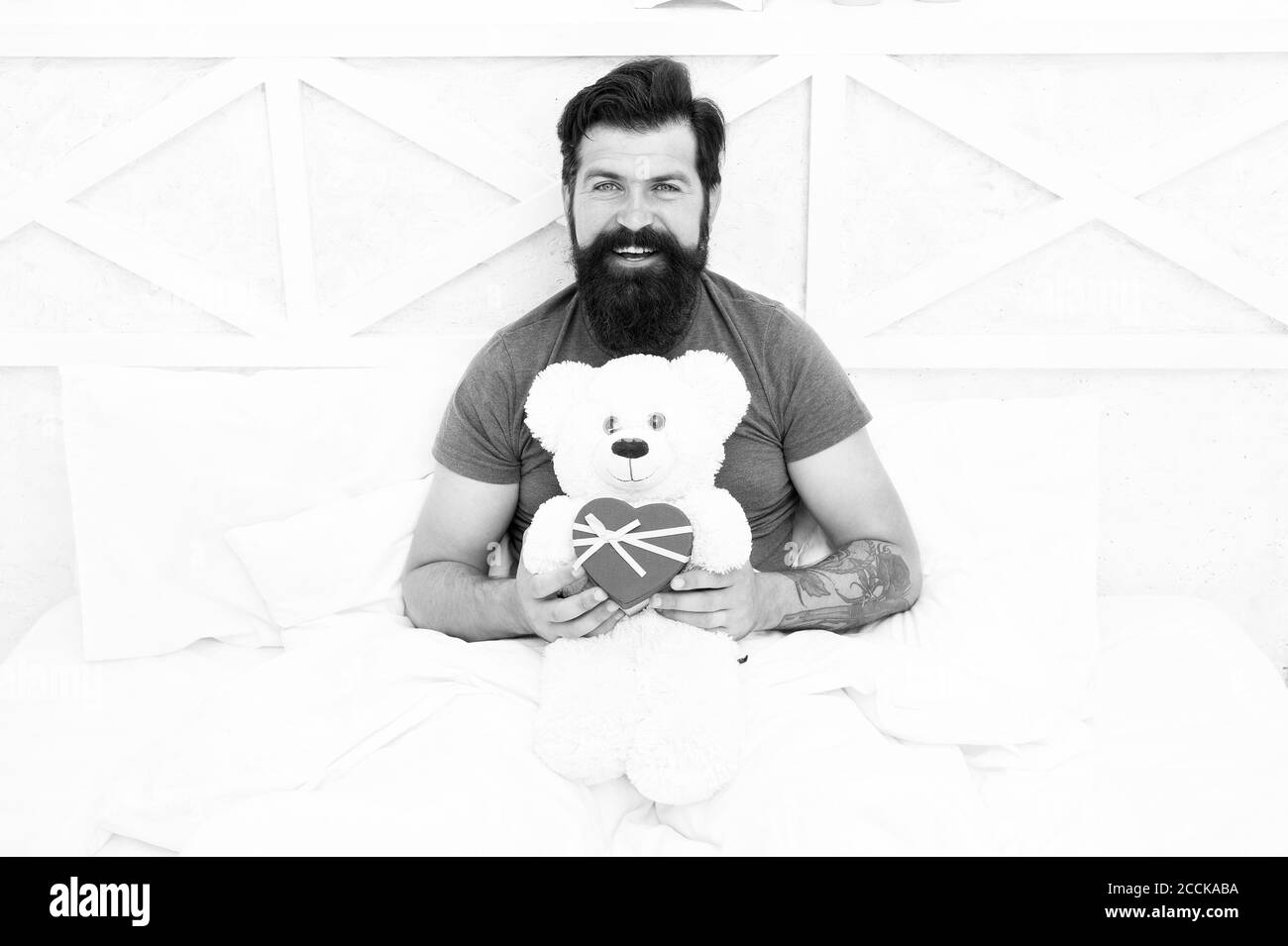 Present for sweetheart. Man hug soft toy relaxing in bed. Make surprise concept. Gift for spouse. Cute and romantic gift. Bearded hipster prepare lovely gift. Valentines day gift. Spread love. Stock Photo