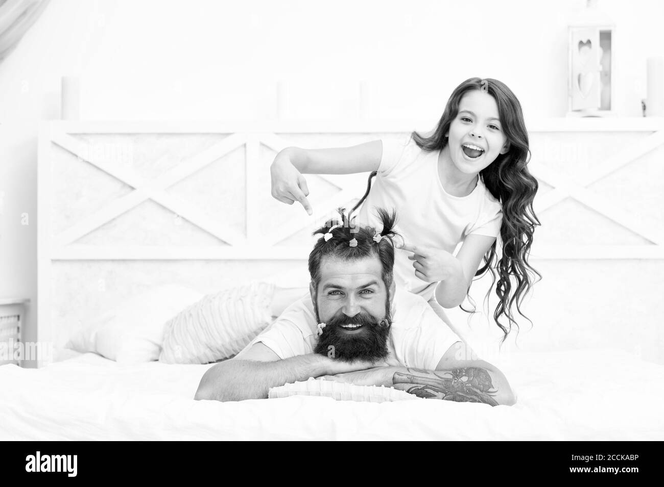 Relaxing in bedroom. Affection and support. Stay home and have fun. Family leisure concept. Girl making hairdo for dad. Quarantine with children. Happy family. Pajamas party. Happy childhood. Stock Photo