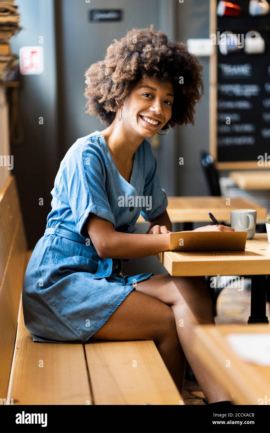 Happy young woman writing in book at table in coffee shop Stock Photo
