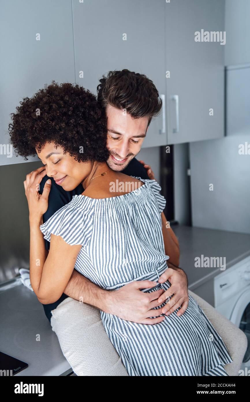Romantic multi-ethnic couple embracing in kitchen of penthouse Stock Photo