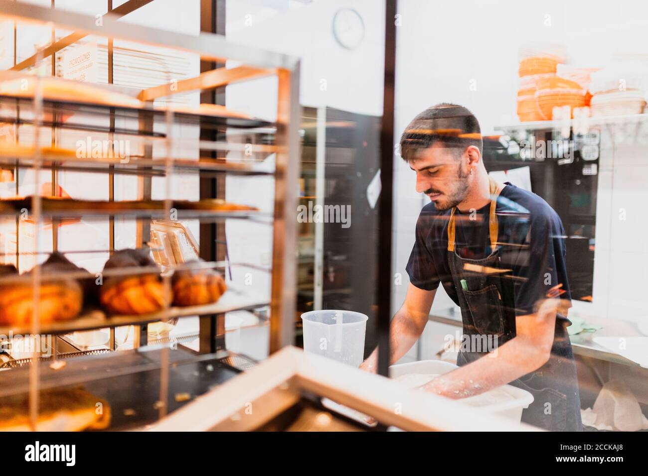Young baker working at bakery seen through glass window Stock Photo Alamy