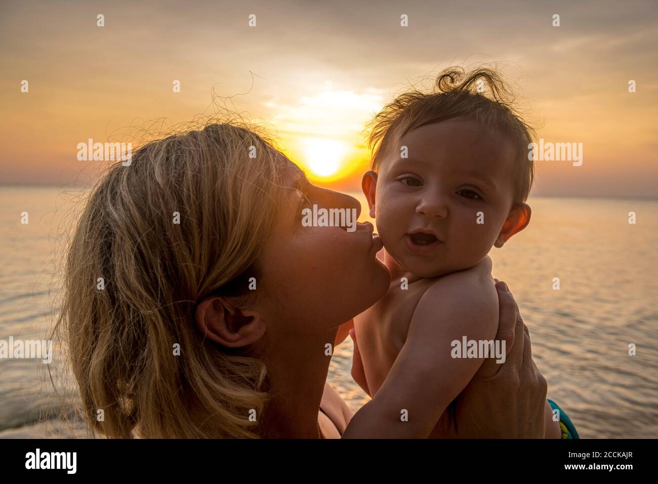 Vietnam, Phu Quoc island, Ong Lang beach, Mother kissing baby in beach at sunset Stock Photo