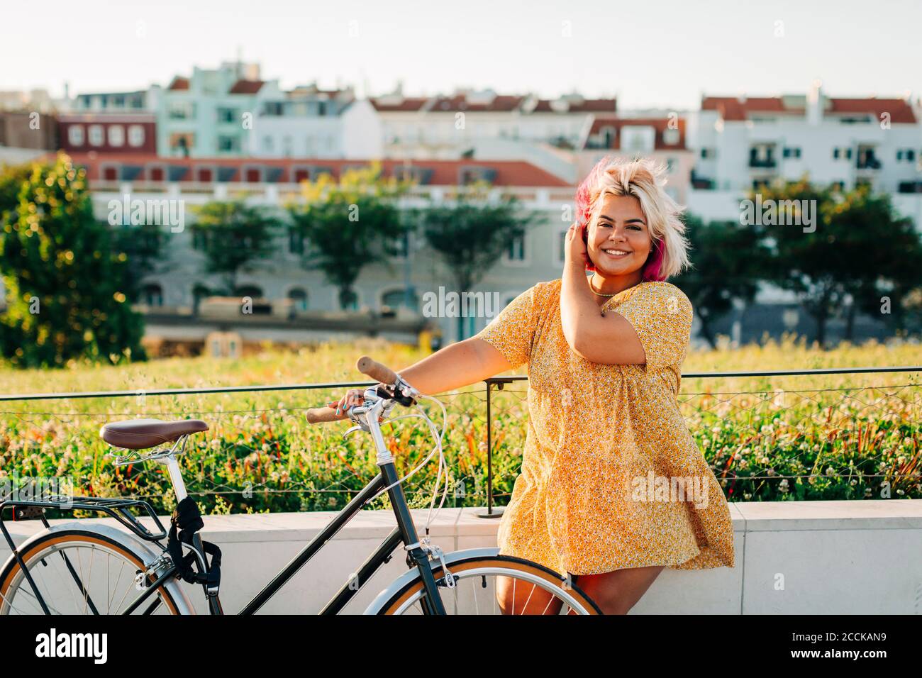 Happy plus size woman with bicycle leaning on park fence Stock Photo