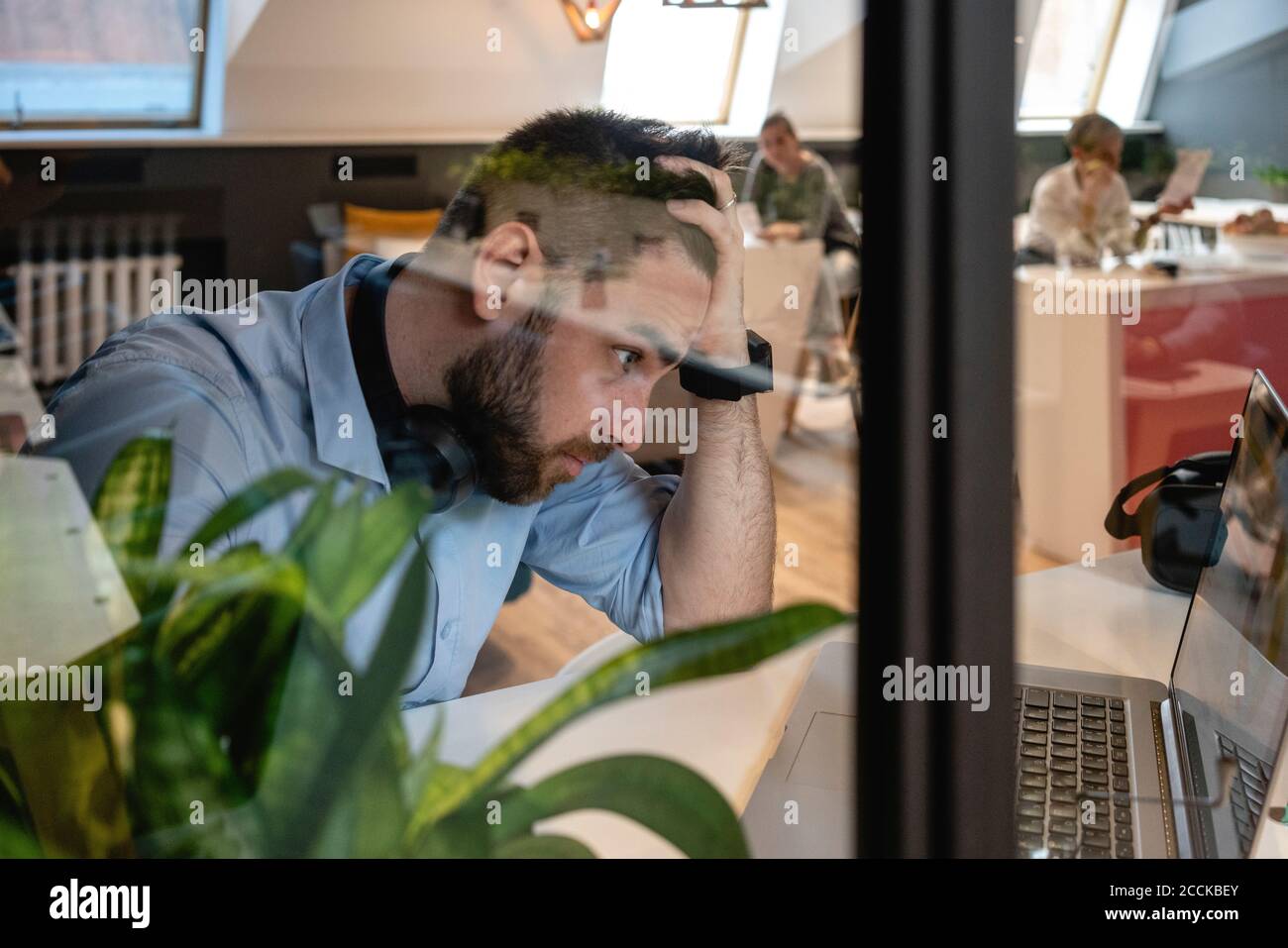 Worried male professional looking at laptop in creative coworking office Stock Photo