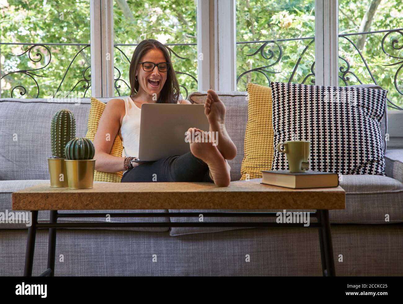 Cheerful woman using laptop while sitting on sofa in living room Stock ...