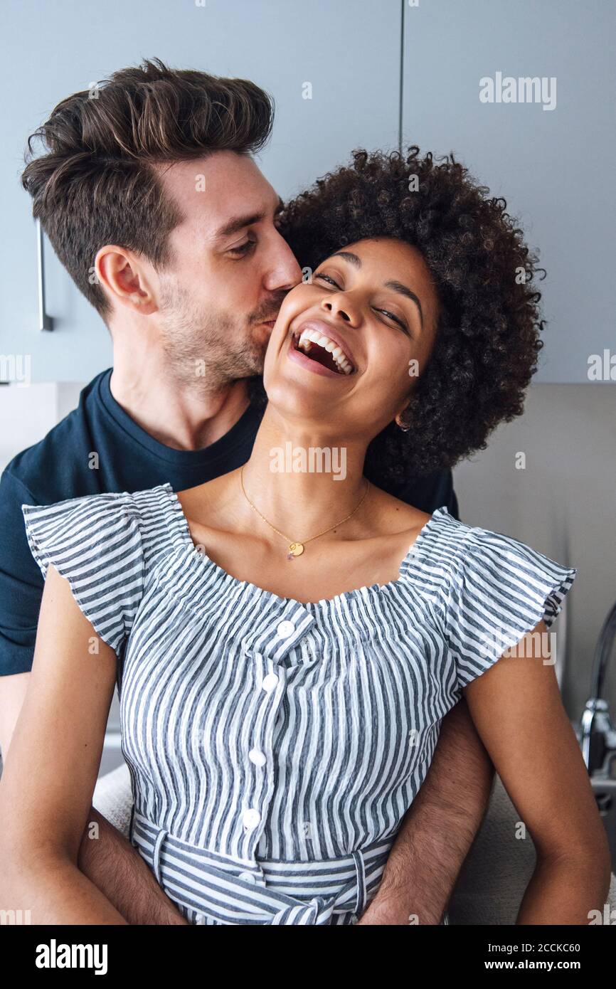 Loving man kissing cheerful woman in kitchen Stock Photo